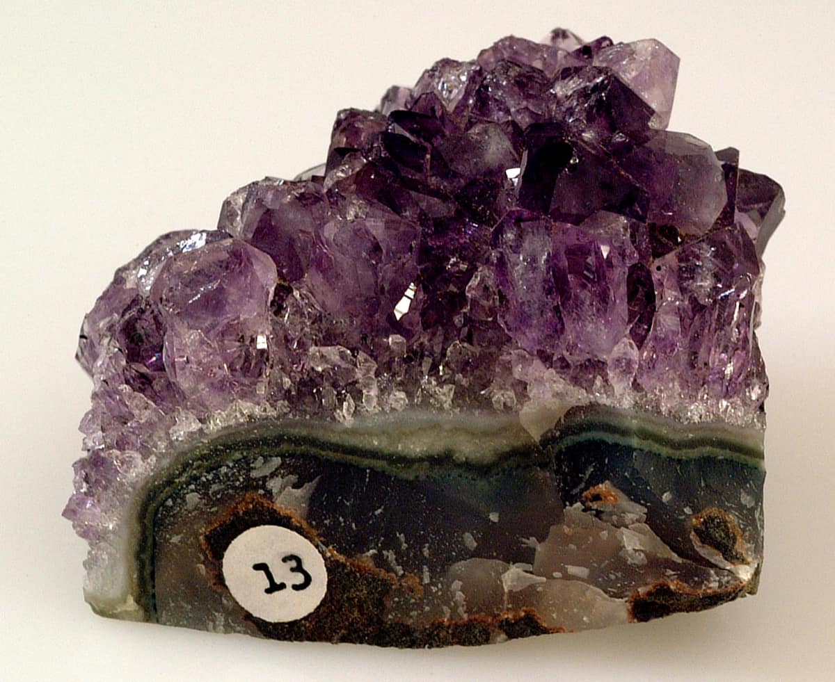 Une tranche de géode d'améthyste : des cristaux violets serrés au-dessus d'une base d'agate rubanée.