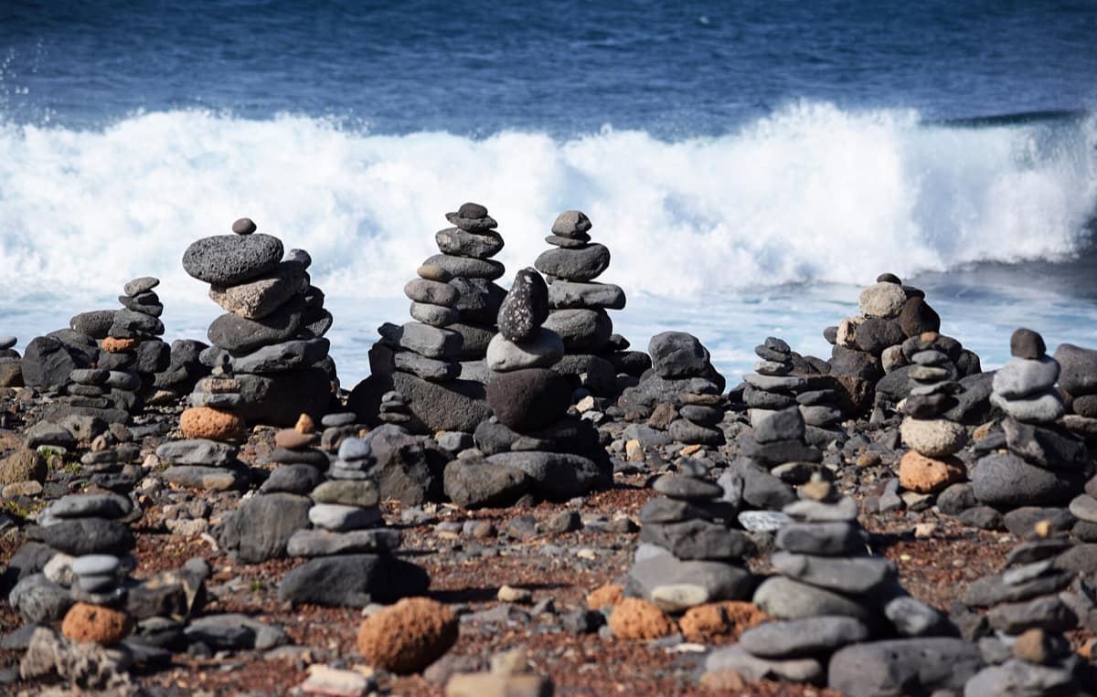 Stacked pebble cairns on a dark volcanic beach, in front of a breaking wave.