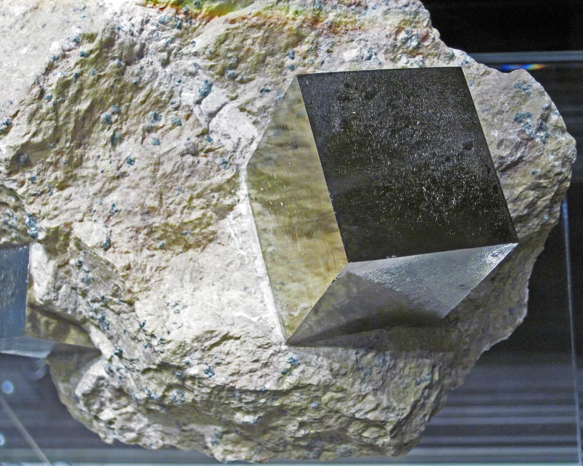 A golden pyrite cube with sharp edges, set into pale marlstone.
